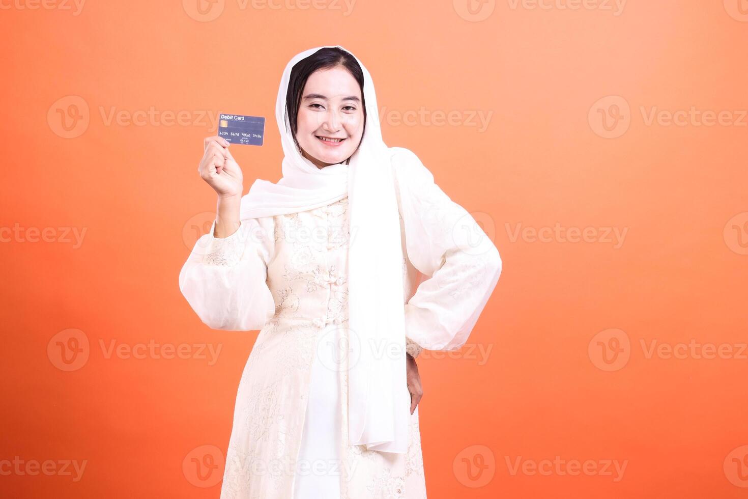 Happy Muslim Woman Displaying Debit Card Enjoy convenient transactions with this smiling woman, isolated on a orange background. photo