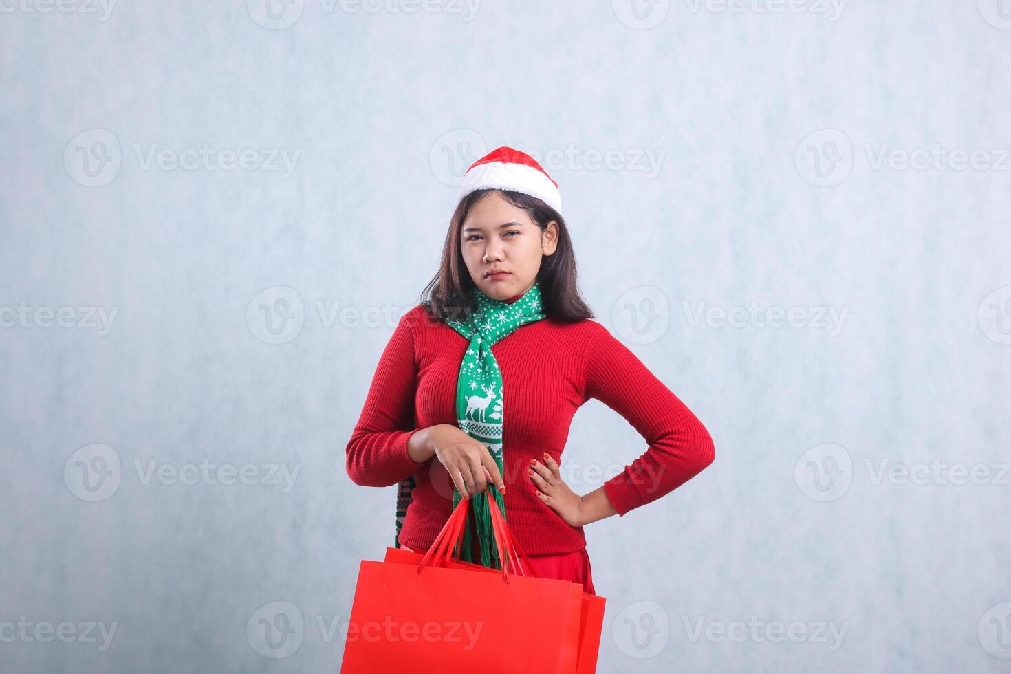 portrait of beautiful ladies wearing christmas sweater, santa hat and scarf, pouting to camera, hand carrying red paper bag of christmas gifts, isolated on white background photo