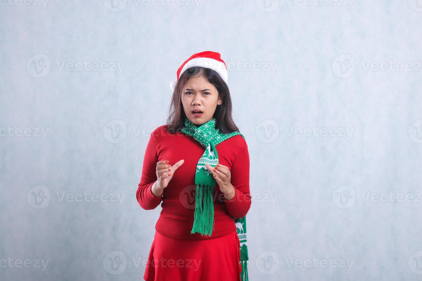 expression of young asian female wearing christmas sweater, santa hat and scarf, annoyed look at front both hands growling, isolated on white background photo