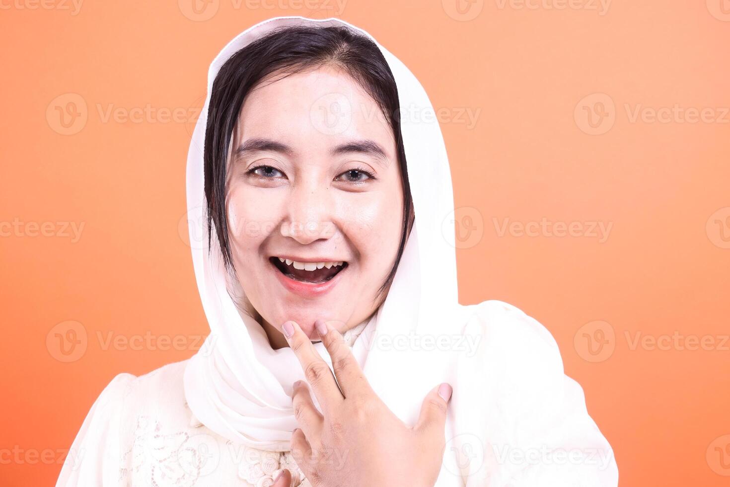 Cheerful Asian Woman in Hijab Smiling Brightly A portrait of a young woman exuding joy and positivity, isolated on a orange background. photo