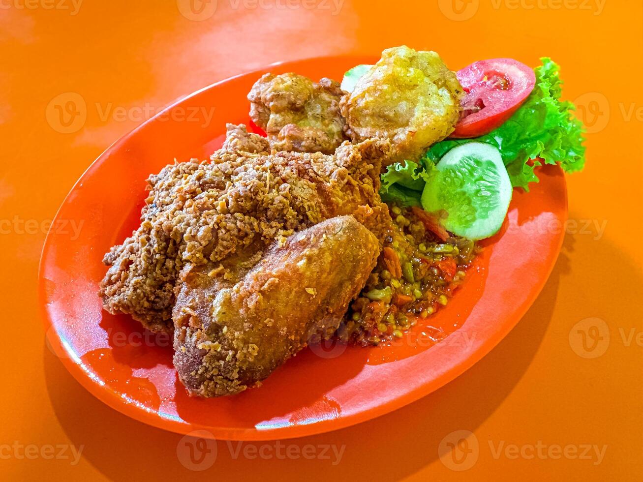 Ayam Geprek with Fried Tofu and Vegetables on Orange Plate photo