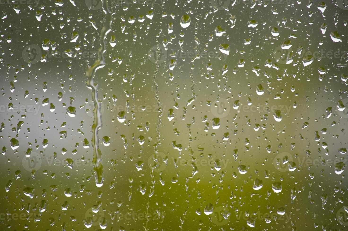 Raindrops cascade down a window, creating a tranquil view with a blurred green backdrop. photo