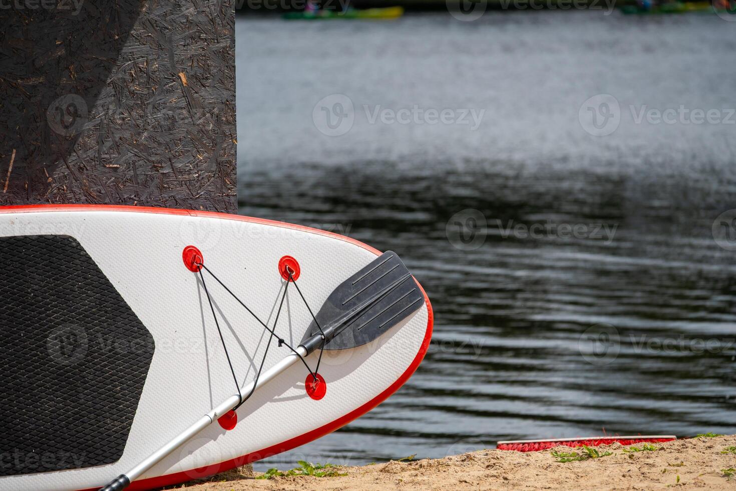 A paddleboard and paddle rest on the sand near calm water, ready for a summer adventure. photo