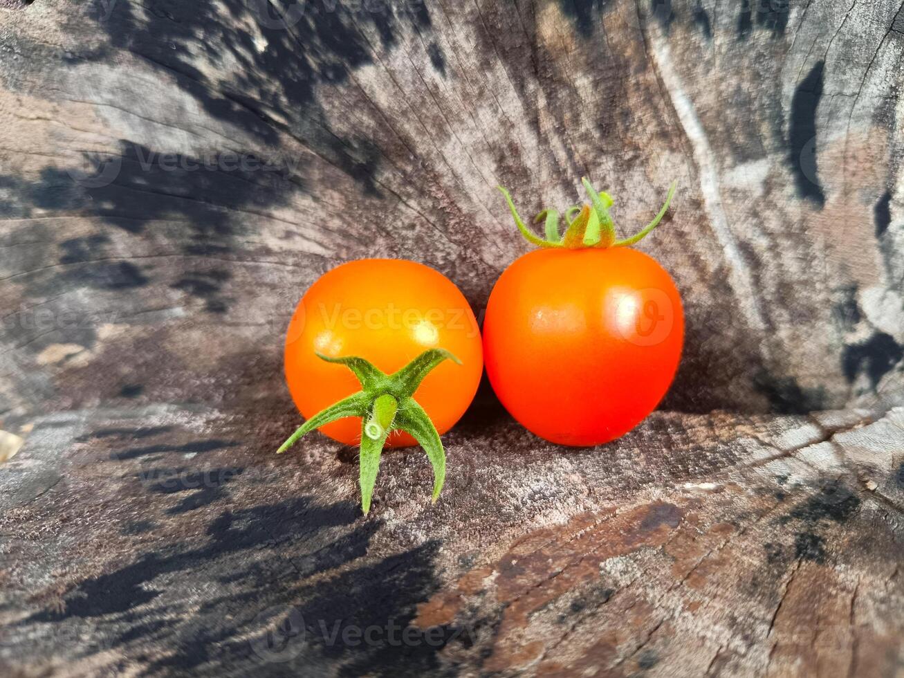 Two orange cherry tomatoes with green stems and petals placed on a wooden surface with a natural texture. photo