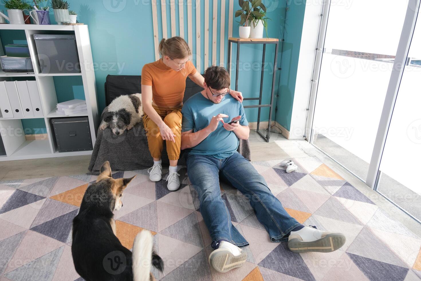 couple sitting on sofa near dog in living room using mobile photo