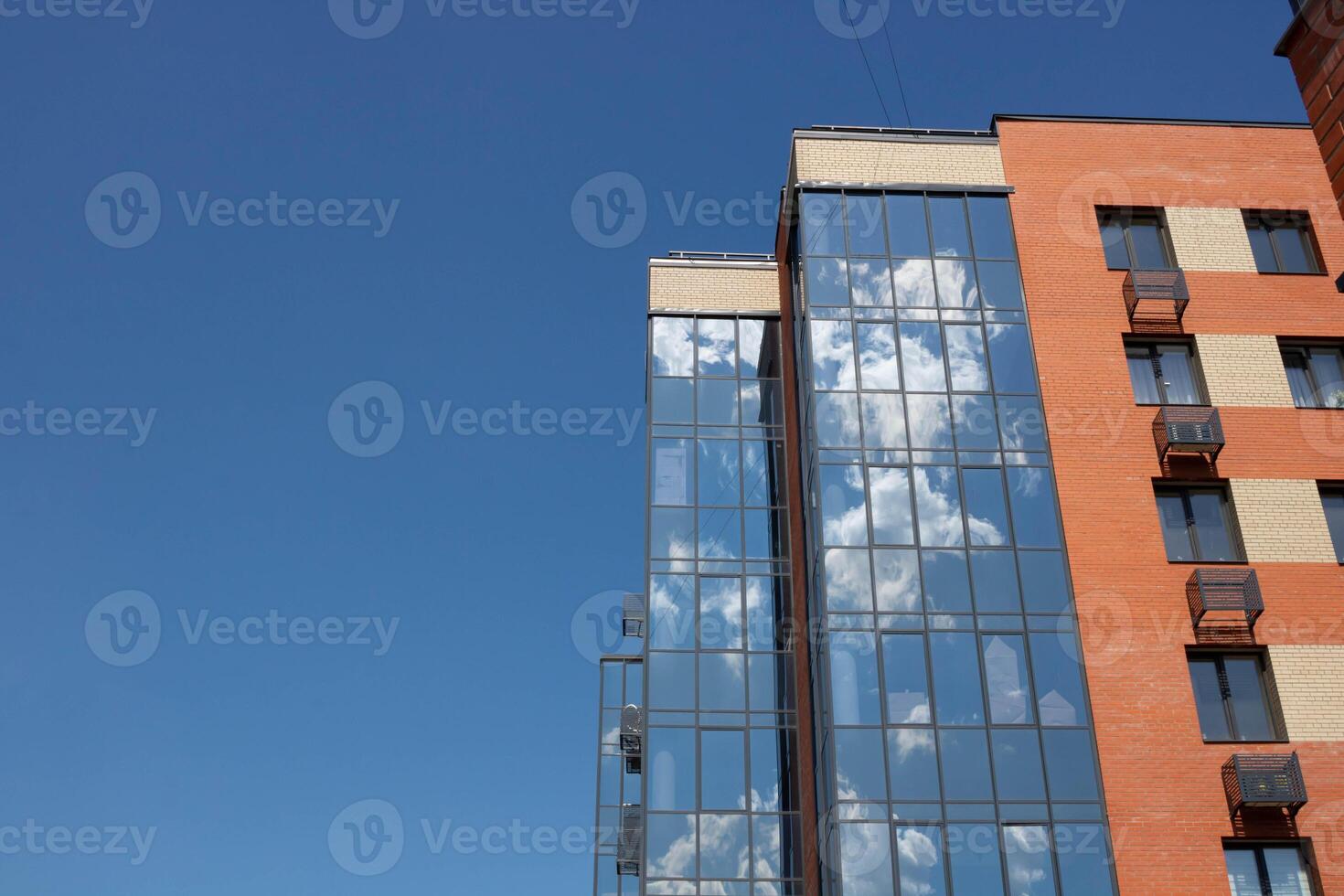 The glass facade of the brick building reflects a blue sky with white clouds photo
