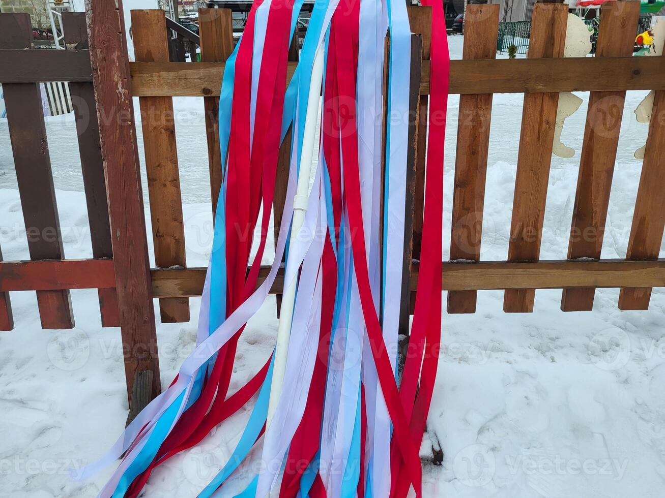 Multicolored white, red, and blue ribbons flutter in the snow on a wooden fence photo