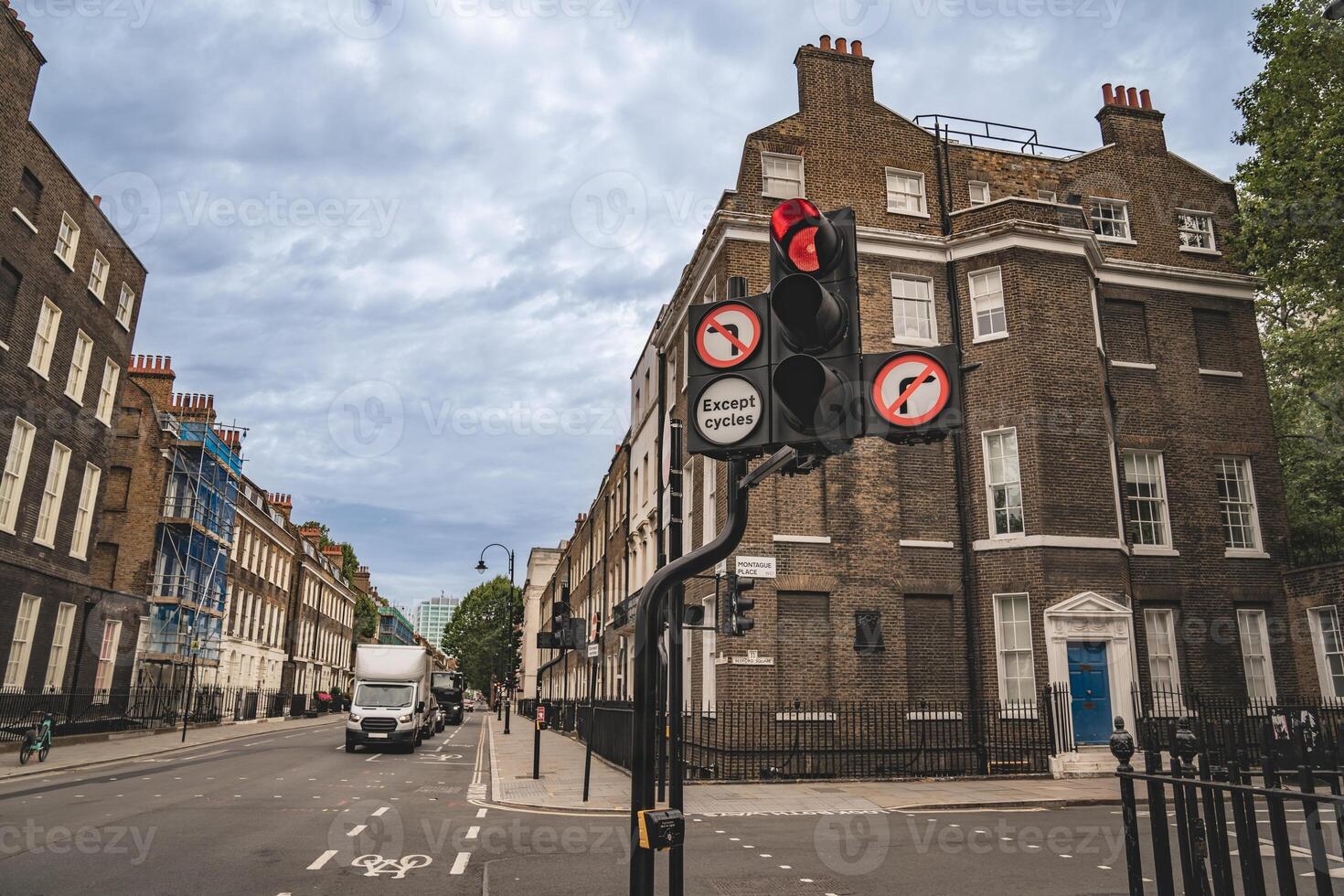 A street in London with a red traffic light and signs indicating no entry except for cycles. The road is lined with classic buildings, and a delivery truck is visible on the street. photo