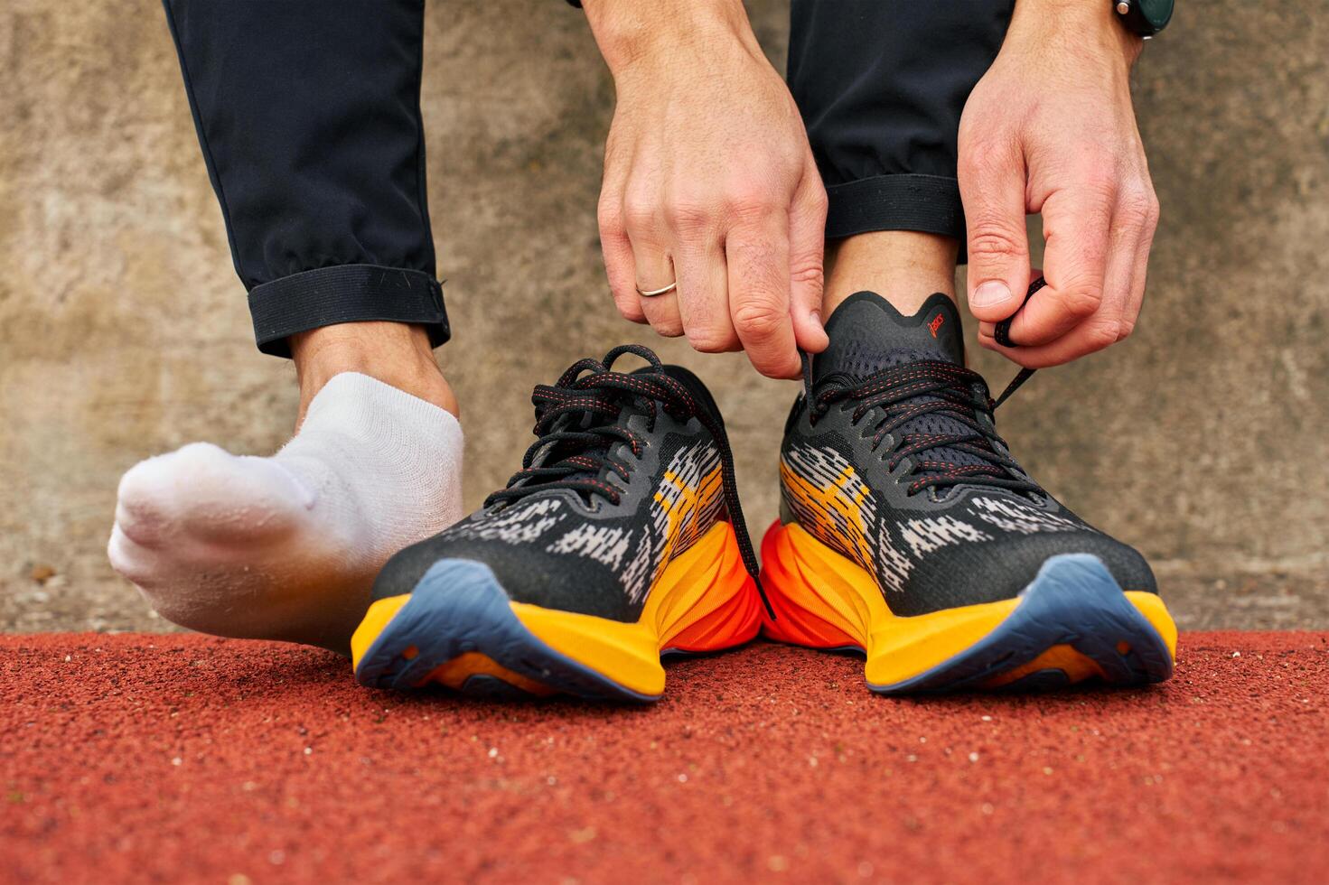 Runner ties shoelaces on black and orange Asics Novablast 3 athletic shoes before training on running track. Sport exercises and an active lifestyle concept. Wroclaw, Poland - November 6, 2024 photo