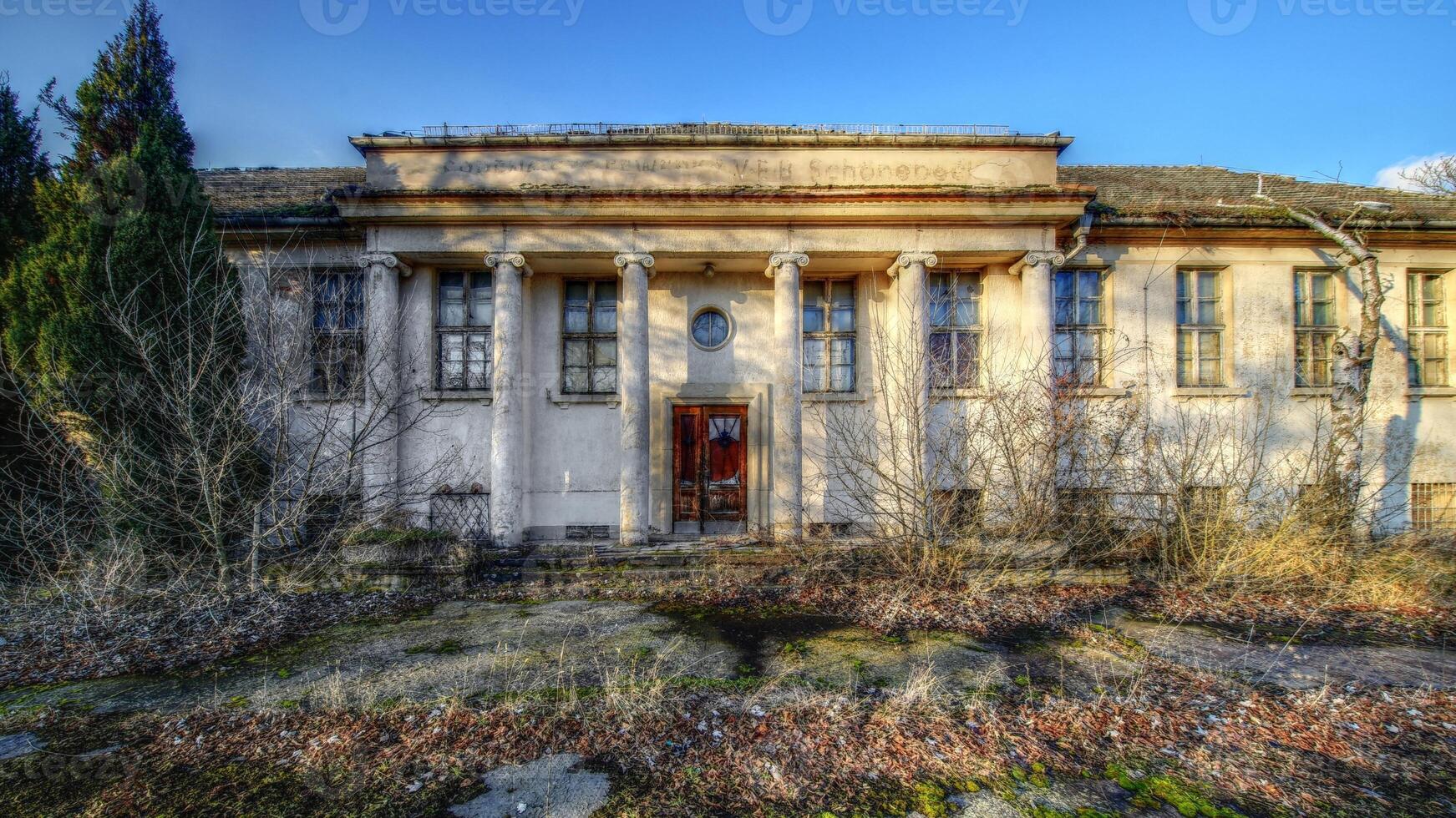Abandoned neoclassical building in Schonebeck, Germany, with weathered columns and vegetation in the foreground photo