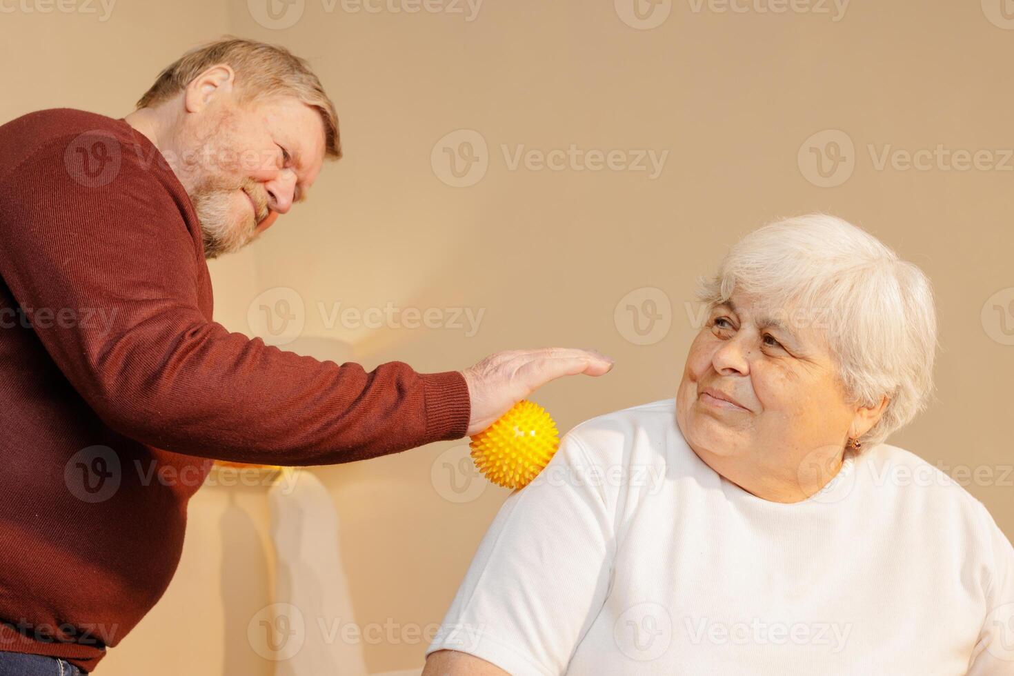 Senior Man Using Spiky Massage Ball for Shoulder Pain Relief and Muscle Therapy on Elderly Woman at Home photo