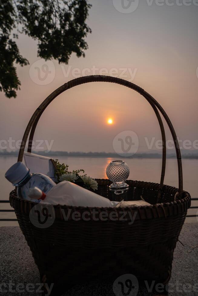 The Stuffs in a wicker basket for offer food or g ive alms to the monks on a stone chair beside Mekong River, Thailand at sunrise time. photo