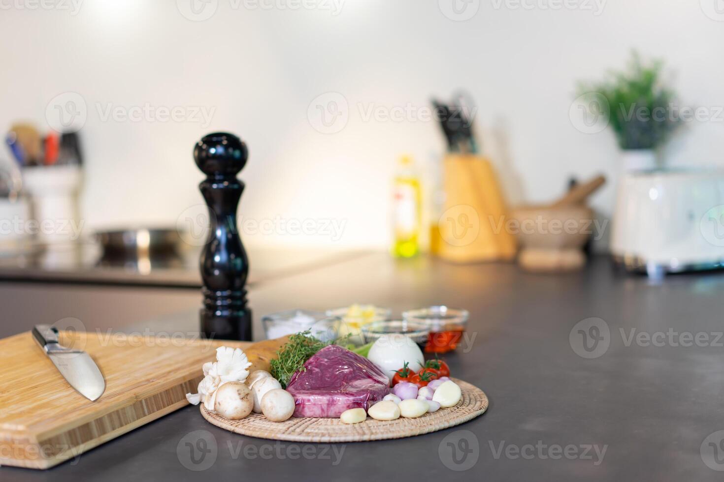 Raw wrap beef steak and variety ingredient on circ le wicker plate with sauce, salt and butter in mini glass bowl on black granite kitchen counter surface. photo