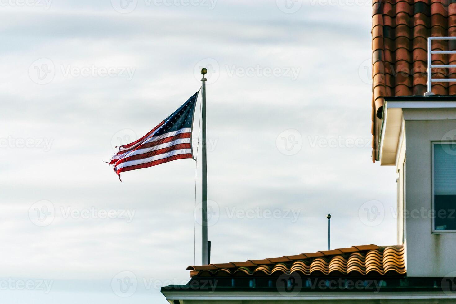 American flag waving on pole near house with tile roof patriotic symbol photo