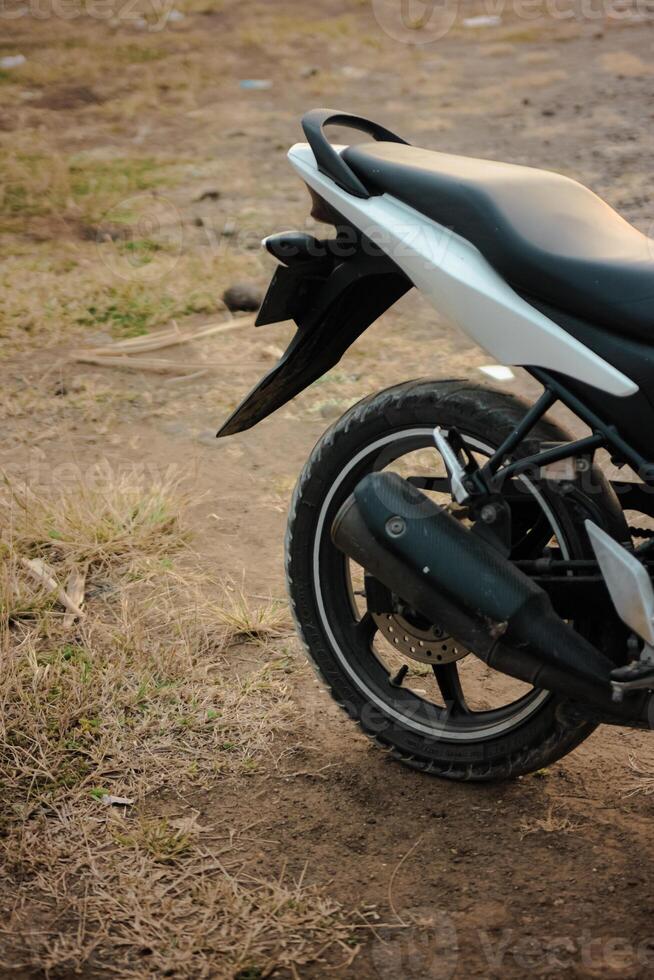 the rear tire and exhaust pipe of a white motorcycle parked on a dirt path. photo