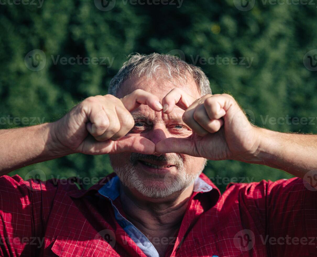 Playful Senior Man Making Heart Shape with Hands in Front of Face photo