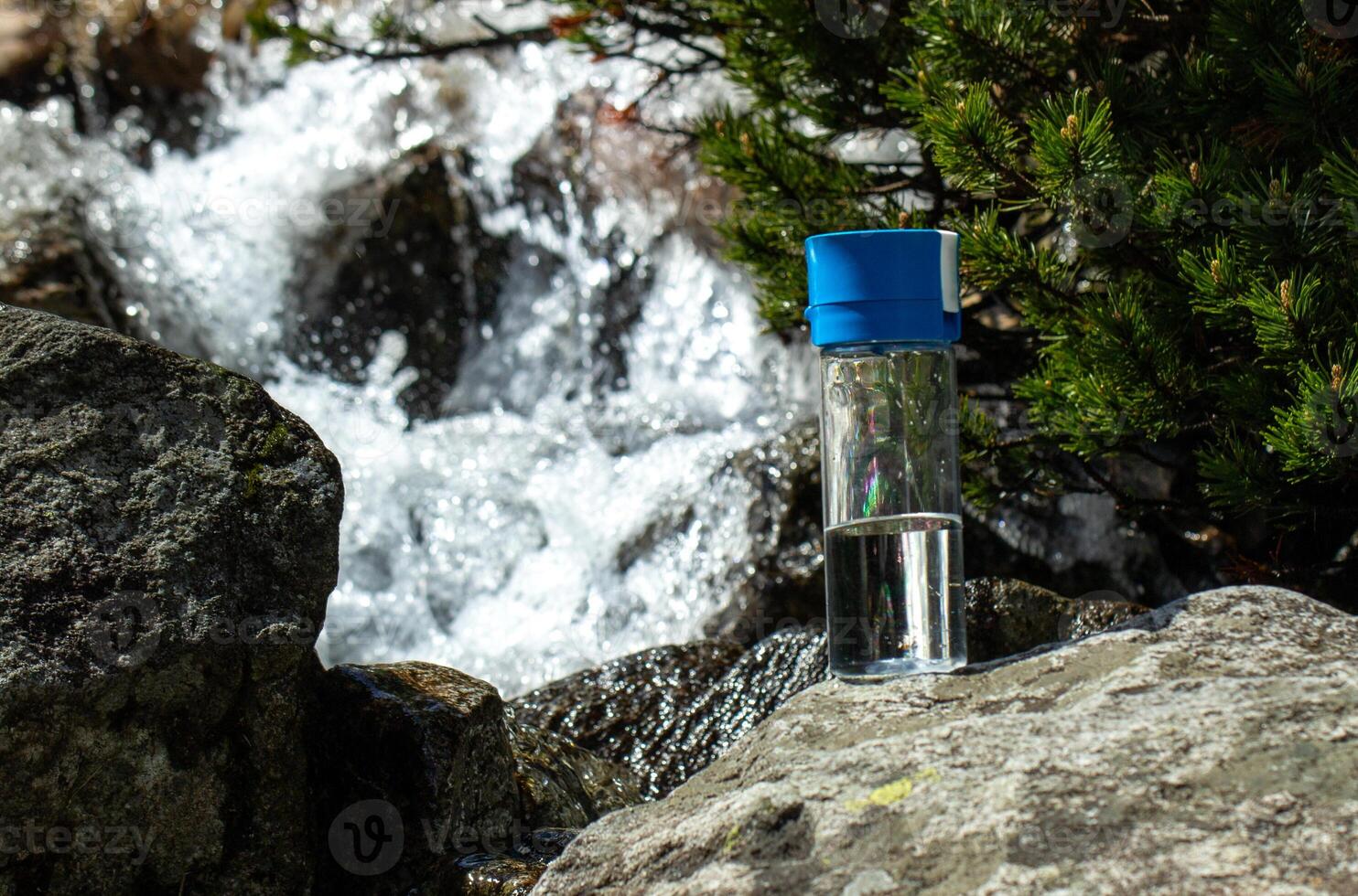 a clear glass bottle on a stone in front of mountain river steam photo