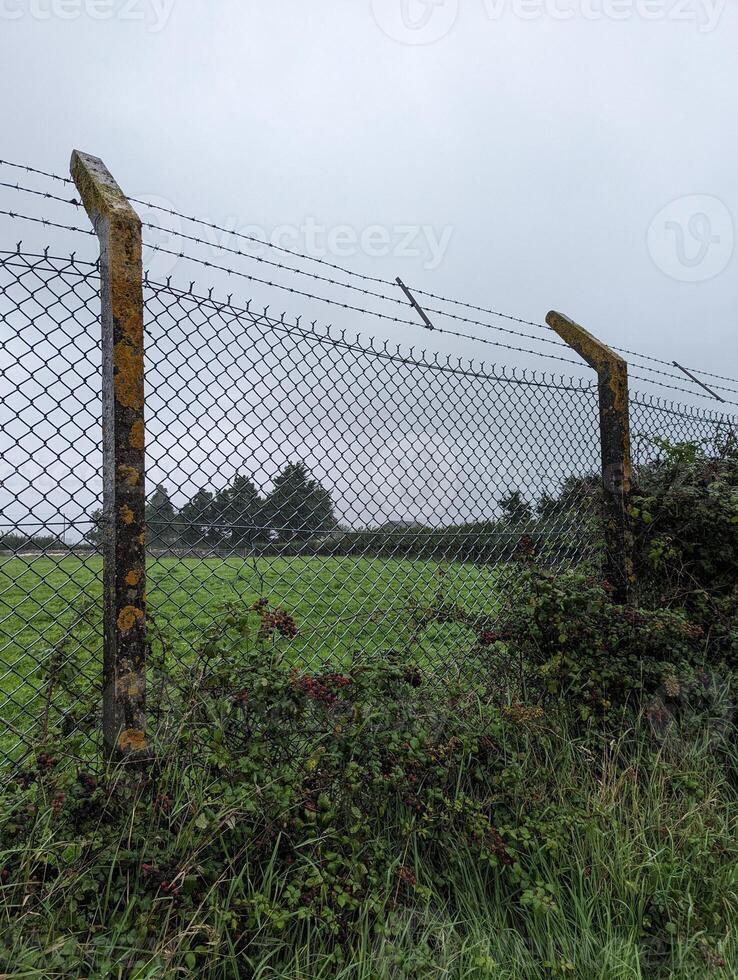 Old Barbed Wire Fence Protecting Farmland with Deteriorating Concrete and Lichen-Covered Posts. photo