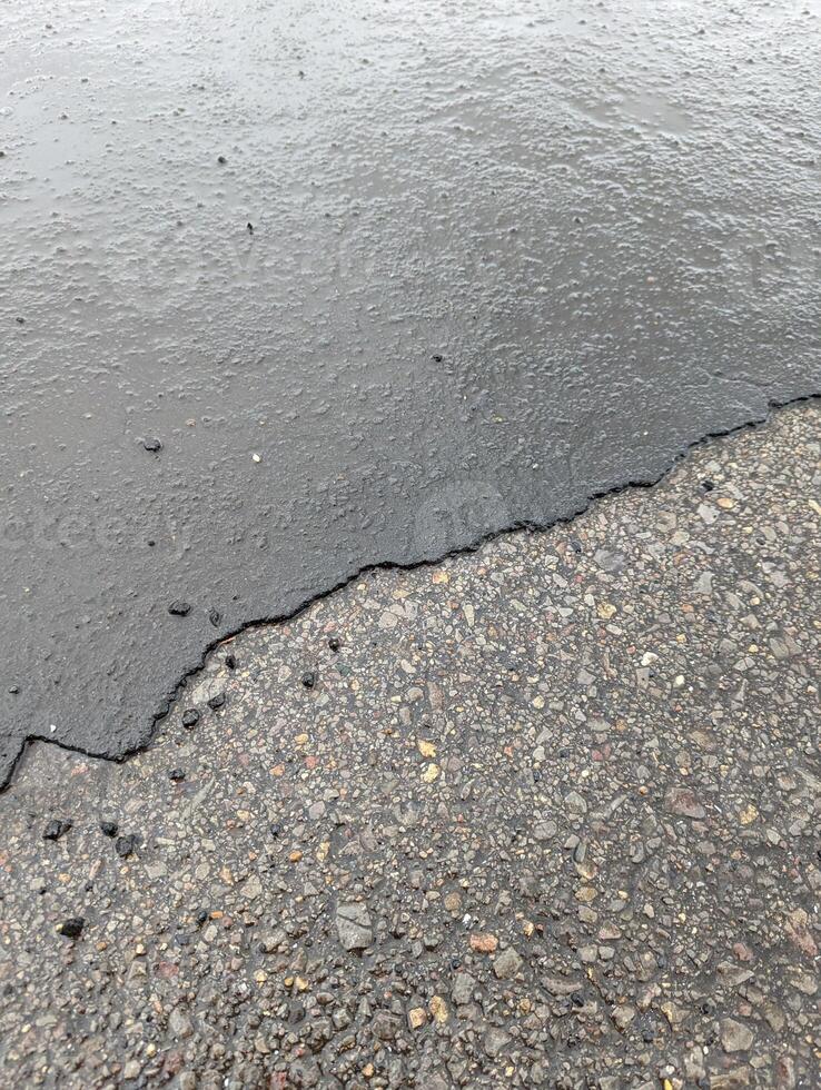 Access road with deteriorating asphalt, gravel, and rainwater accumulation in Wales. photo