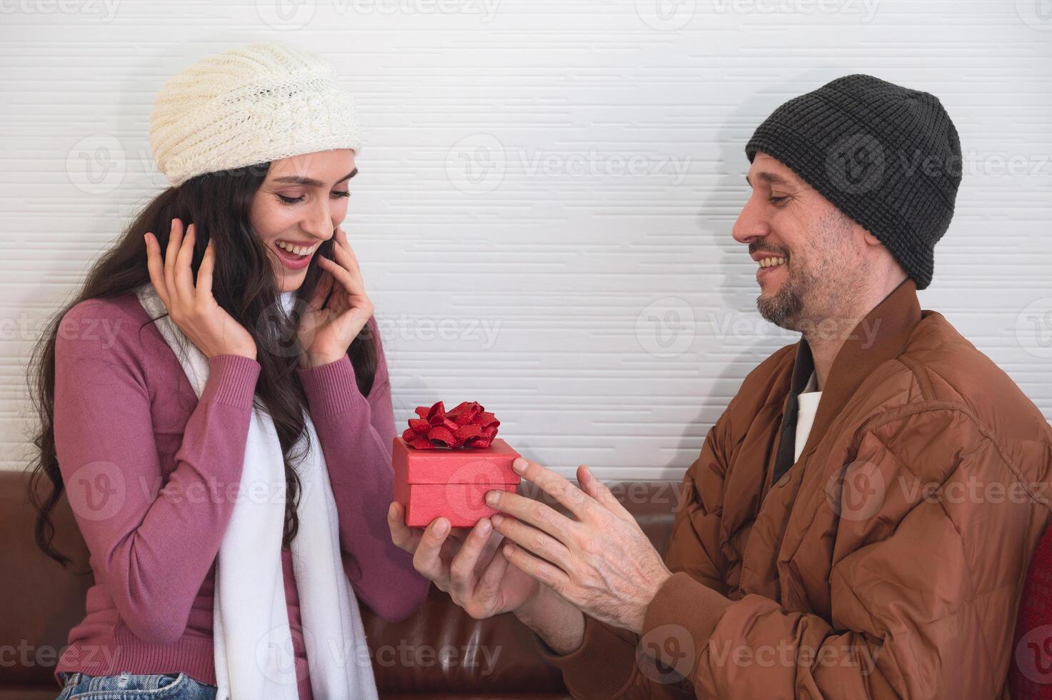 Smiling young woman with husband looking at Christmas gift on sofa in living room photo