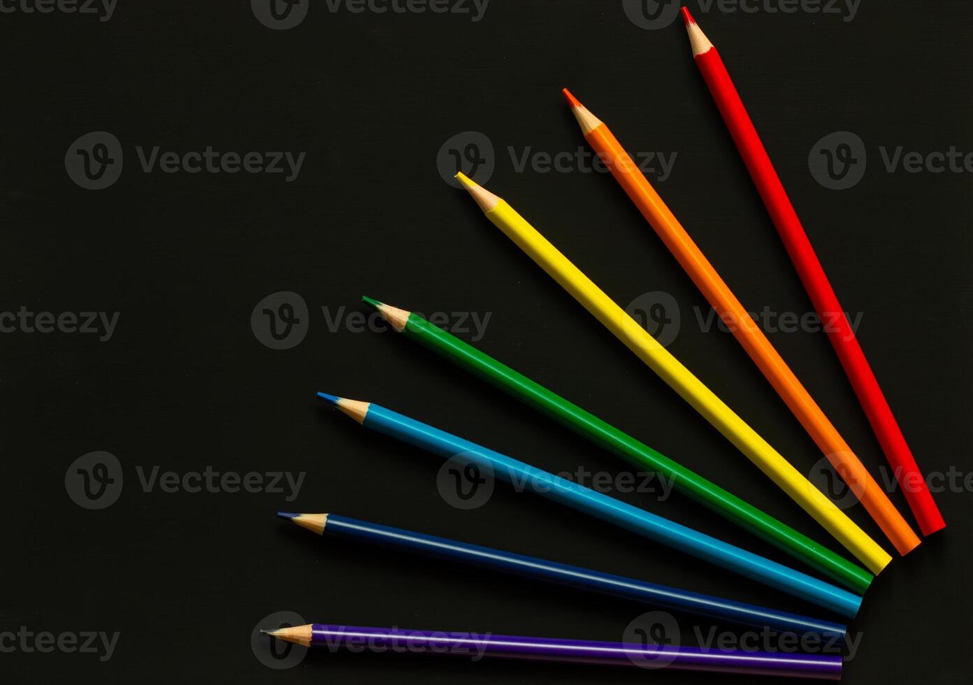 Bright school supplies on plain background. Assortment of colorful stationery, pencil, set of colored pencils, rainbow color order on dark background photo