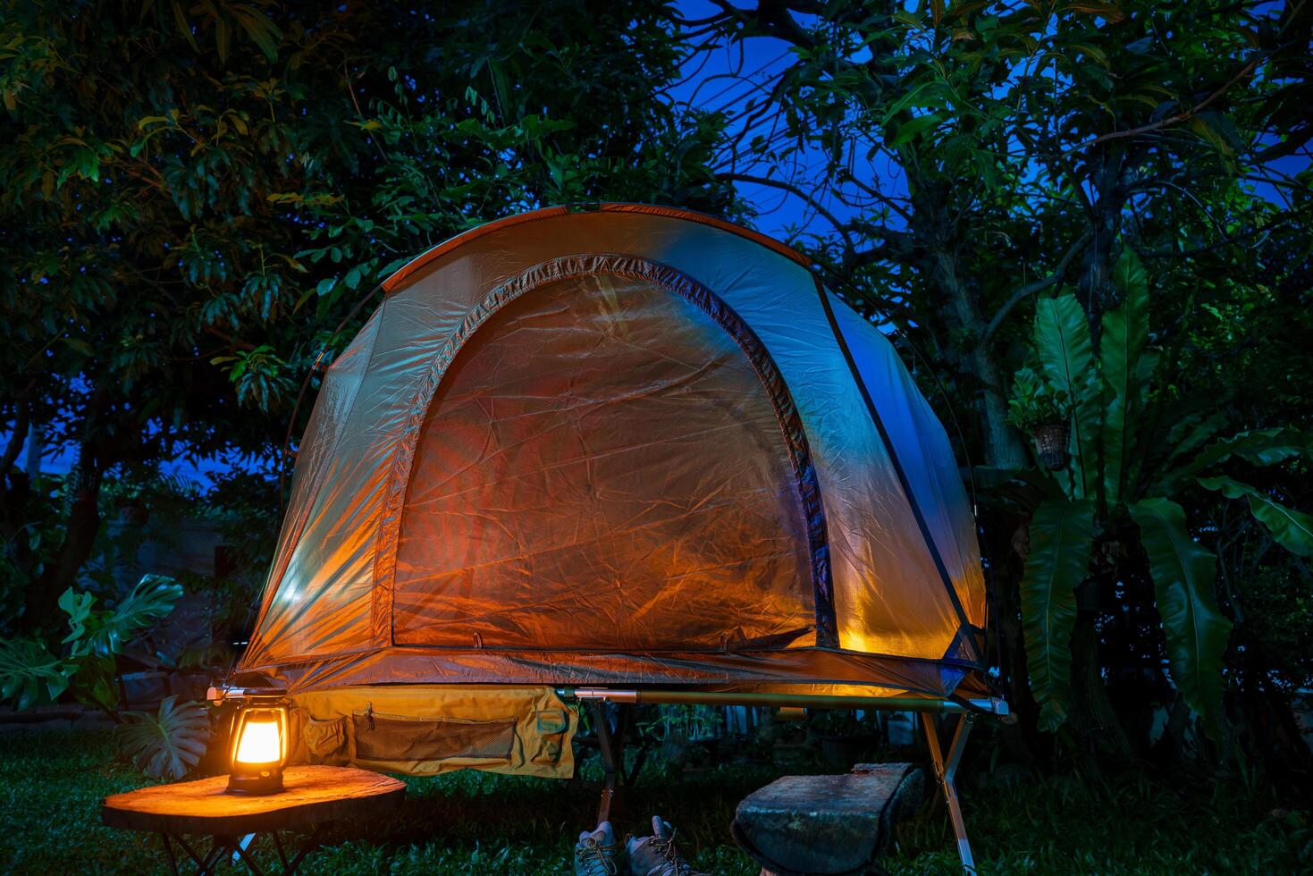 Camping tent and lantern with wooden table in a forest at night photo