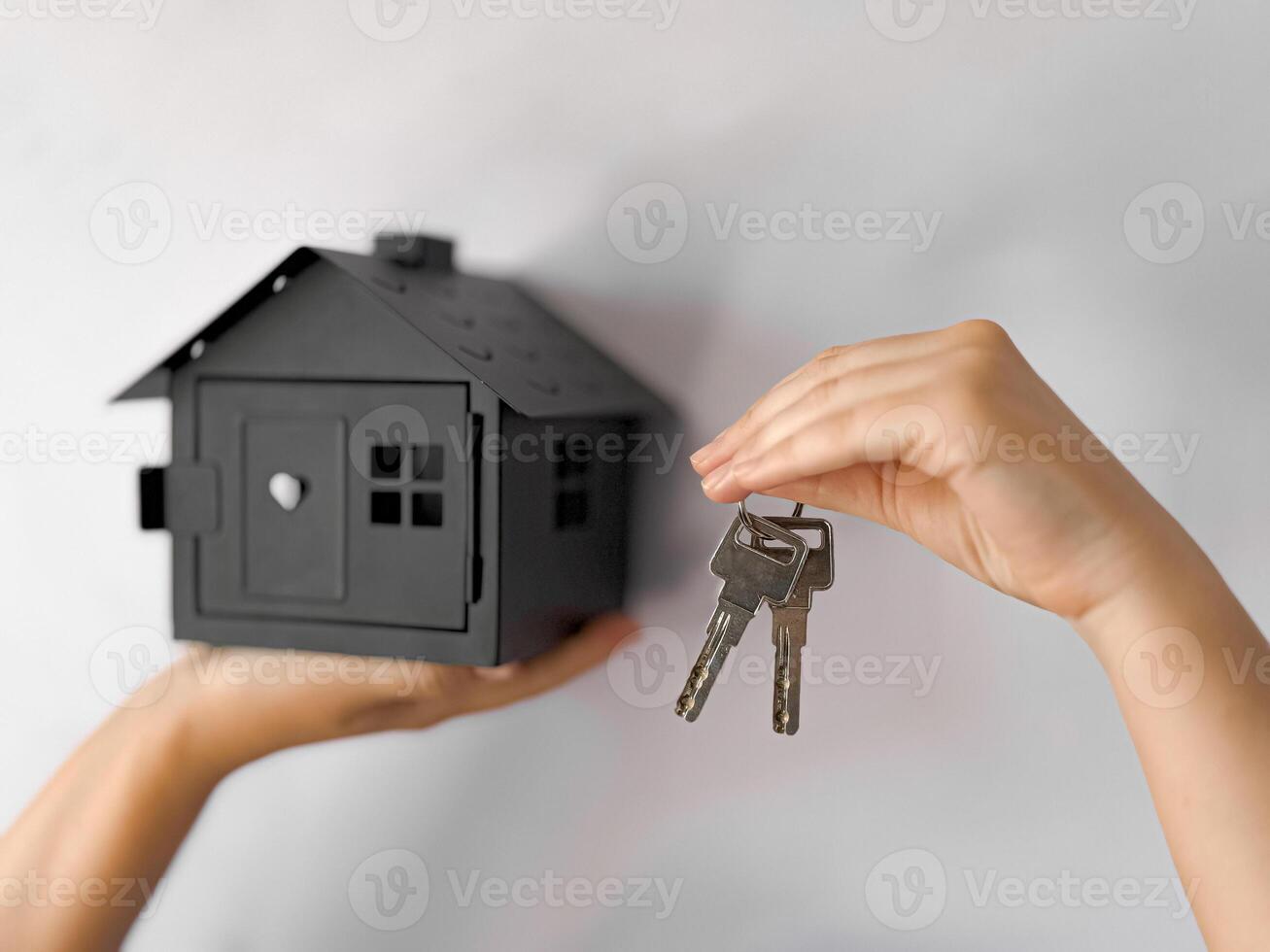Close up of hands holding black house model and keys against light background. Concept of real estate, home ownership, or investment. Minimalist and modern representation of buying. photo