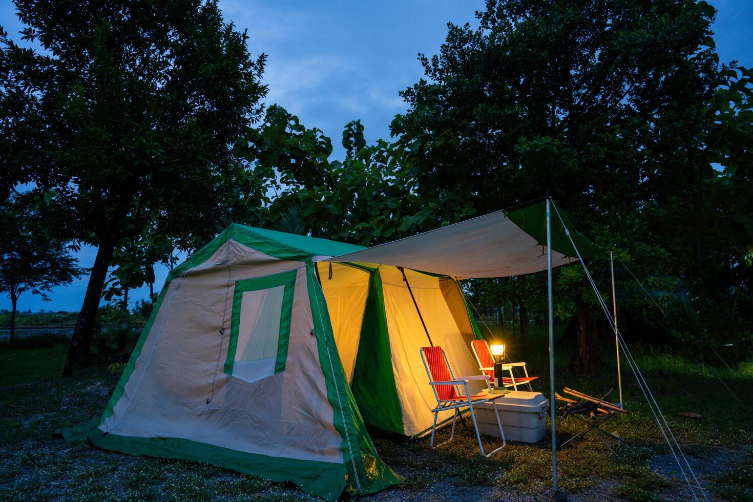Camping tents at night, vintage cabin tents, Antique lanterns, retro chairs, and outdoor coffee-making facilities on wooden tables in a forest photo