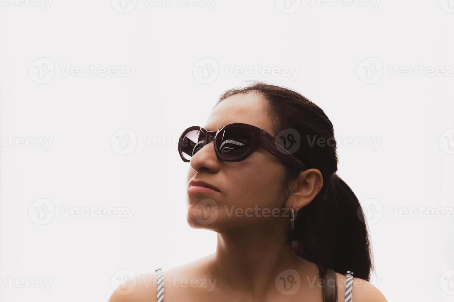 Woman with glasses and in front of a white background looks up in profile. photo