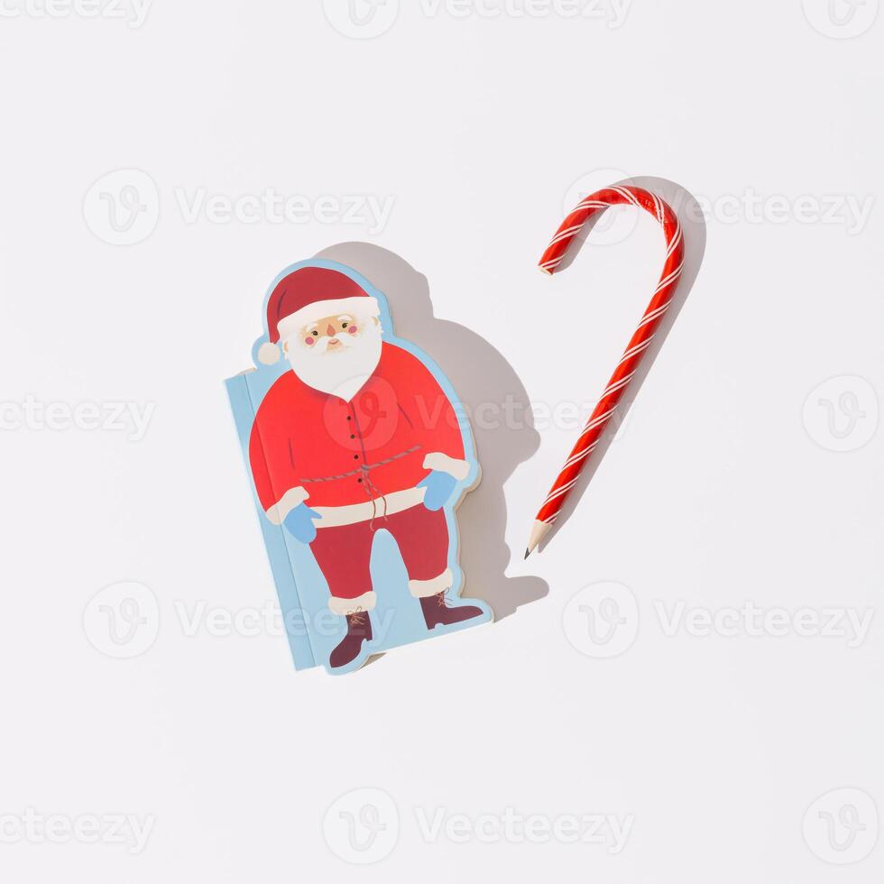 Christmas scene made with candy cane pencil and Santa Claus notebook on white background. Minimal Christmas and New Year concept. Writing letters to Santa idea. Xmas aesthetic. Flat lay. photo