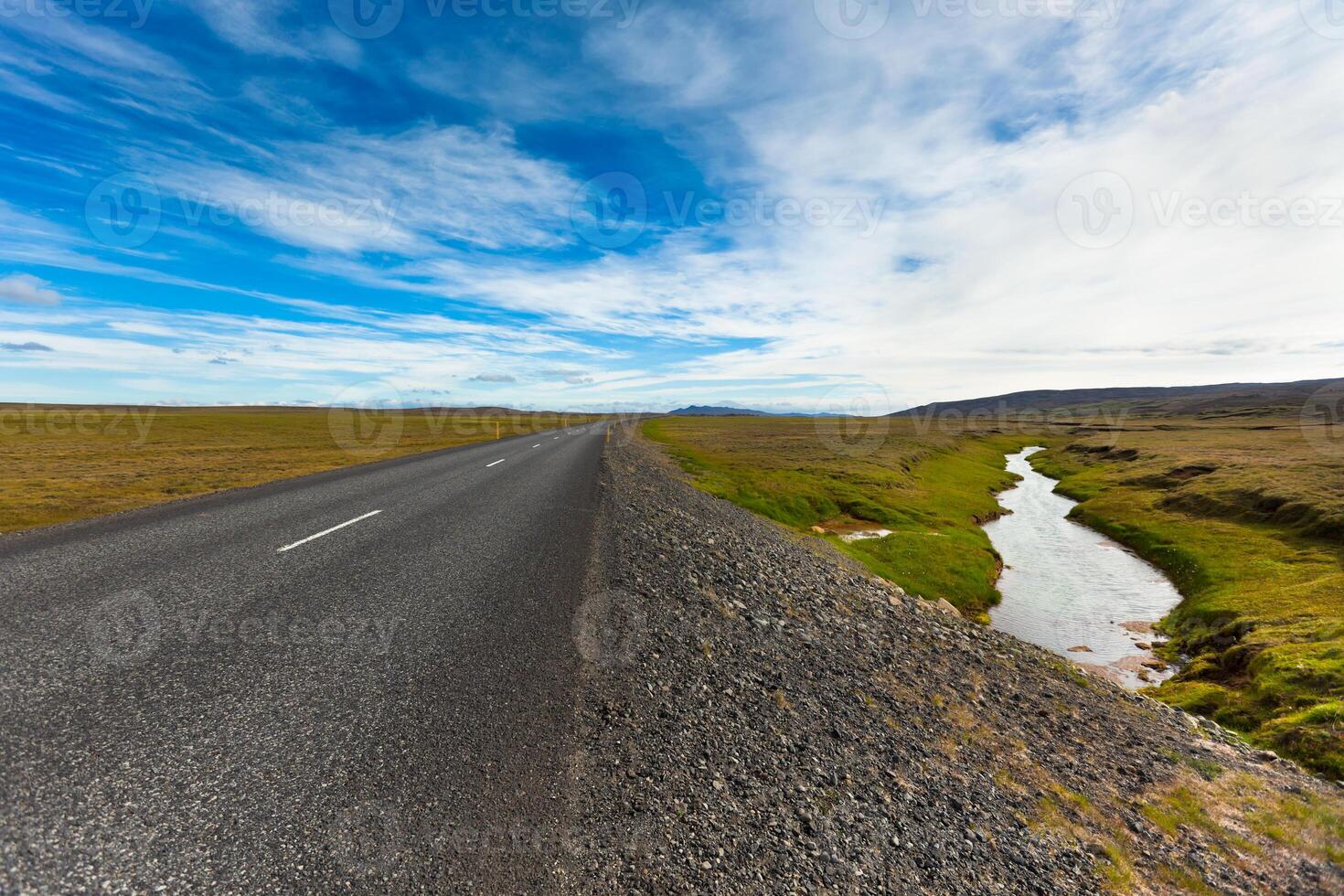 Highway through Icelandic landscape under a blue summer sky with clouds photo