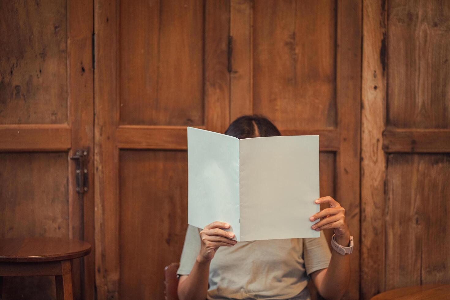 Close up teenage girl holding and reading mock up book or magazine in reading room with wood wall at home, copy space concept. photo