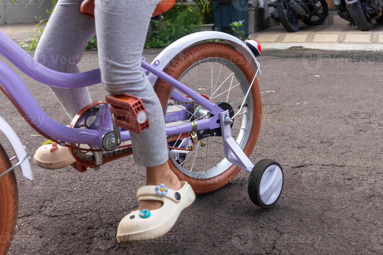 Little girl riding her bicycle with training wheels on the street in front of her house photo