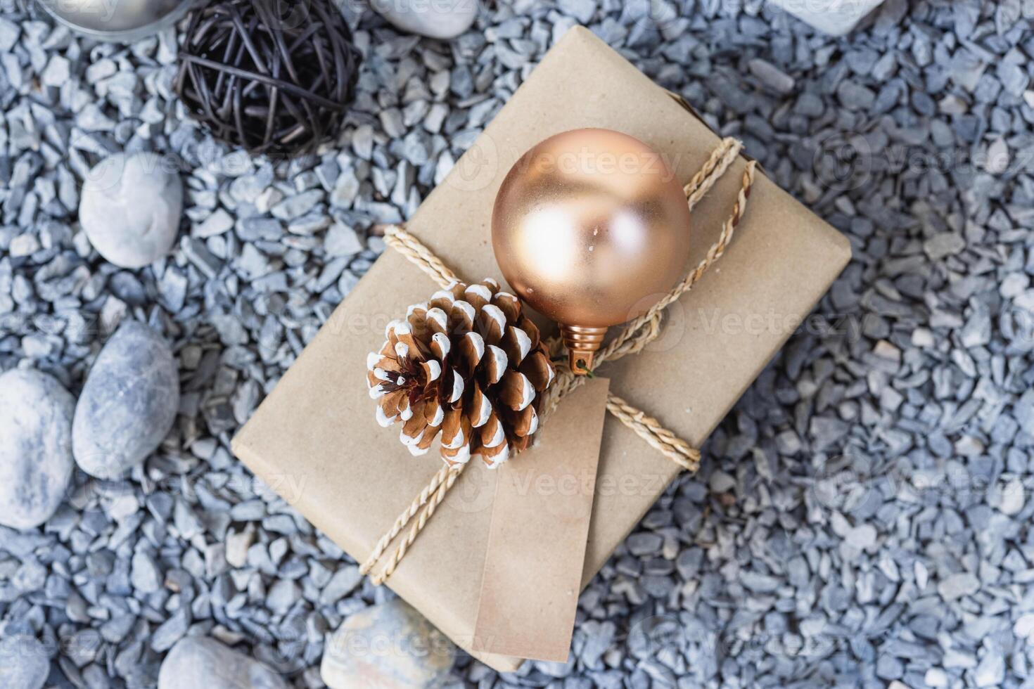 Gift box with gold christmas ball and pine cone on stone background photo