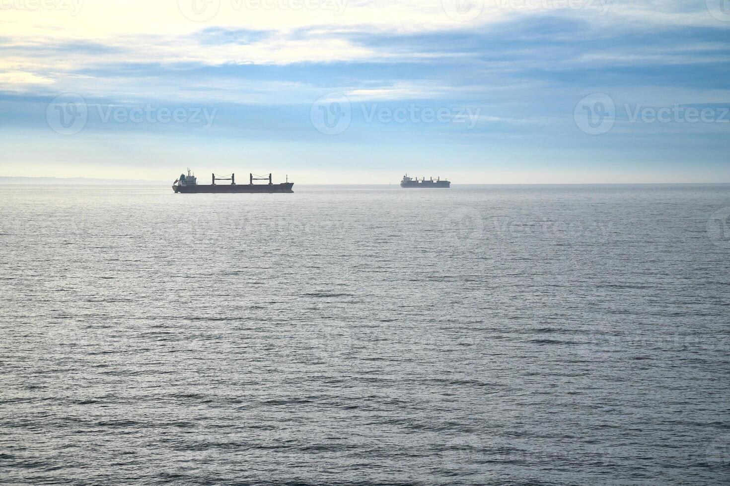 Two cargo ships glide across a calm sea under a clear sky. Minimalist seascape. photo