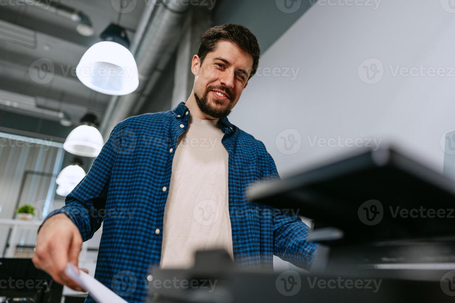 Man using a printer in a modern office space during working hours with bright overhead lighting photo