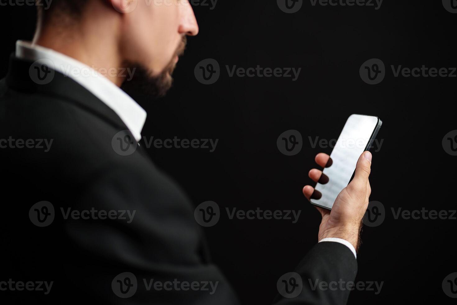 Man in formal attire checking smartphone against a dark background in a modern setting photo