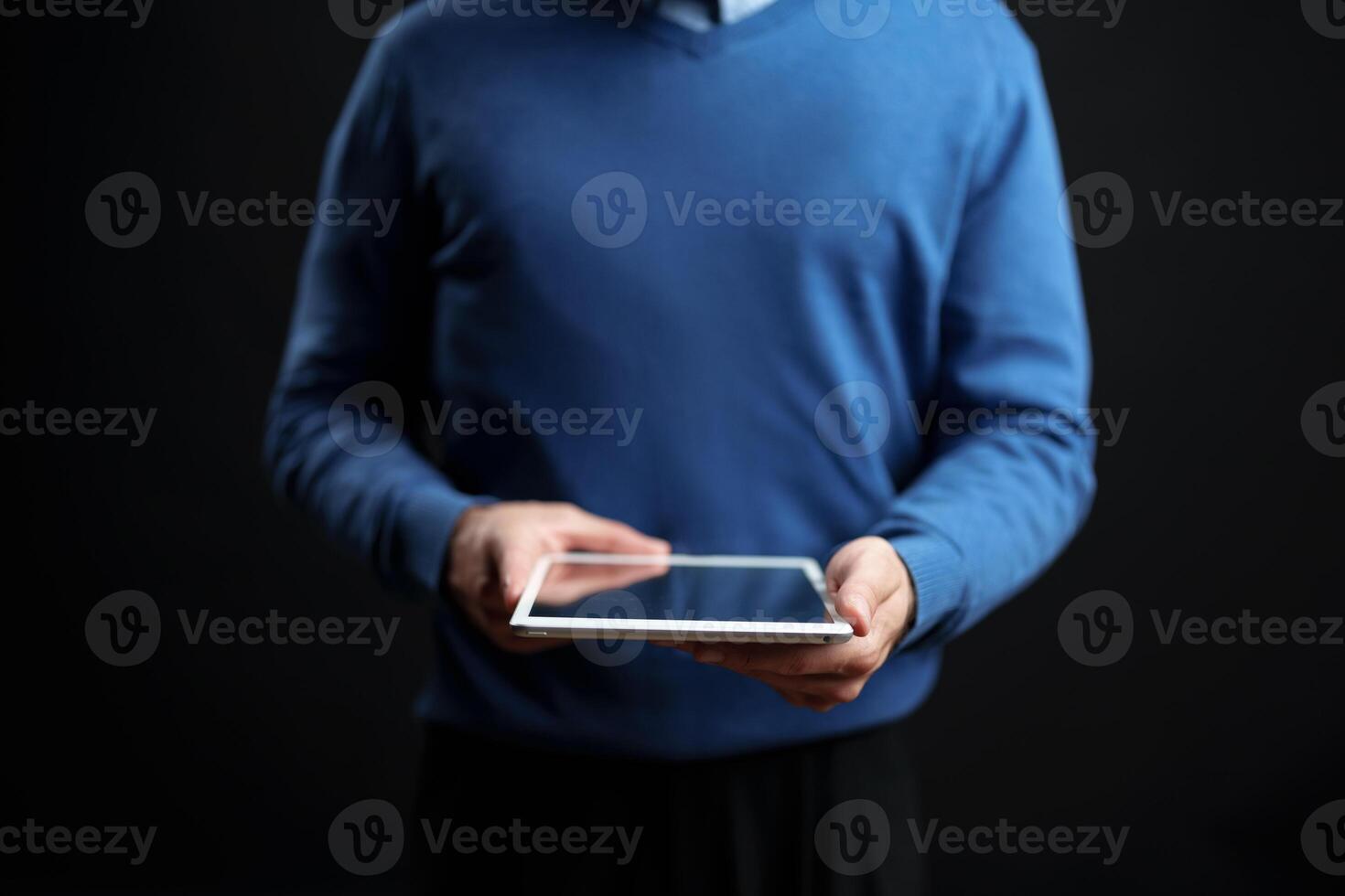 Person using a tablet while standing against a dark background during an indoor setting in a casual environment photo