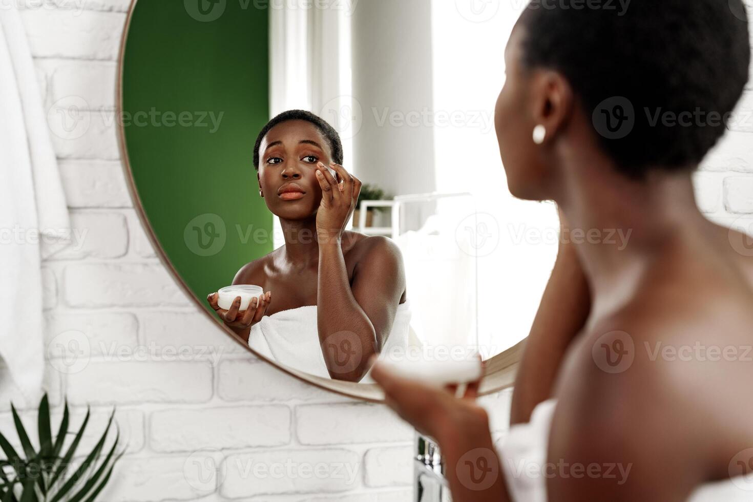 Skincare routine of a woman applying cream in a modern bathroom mirror during the evening hours photo