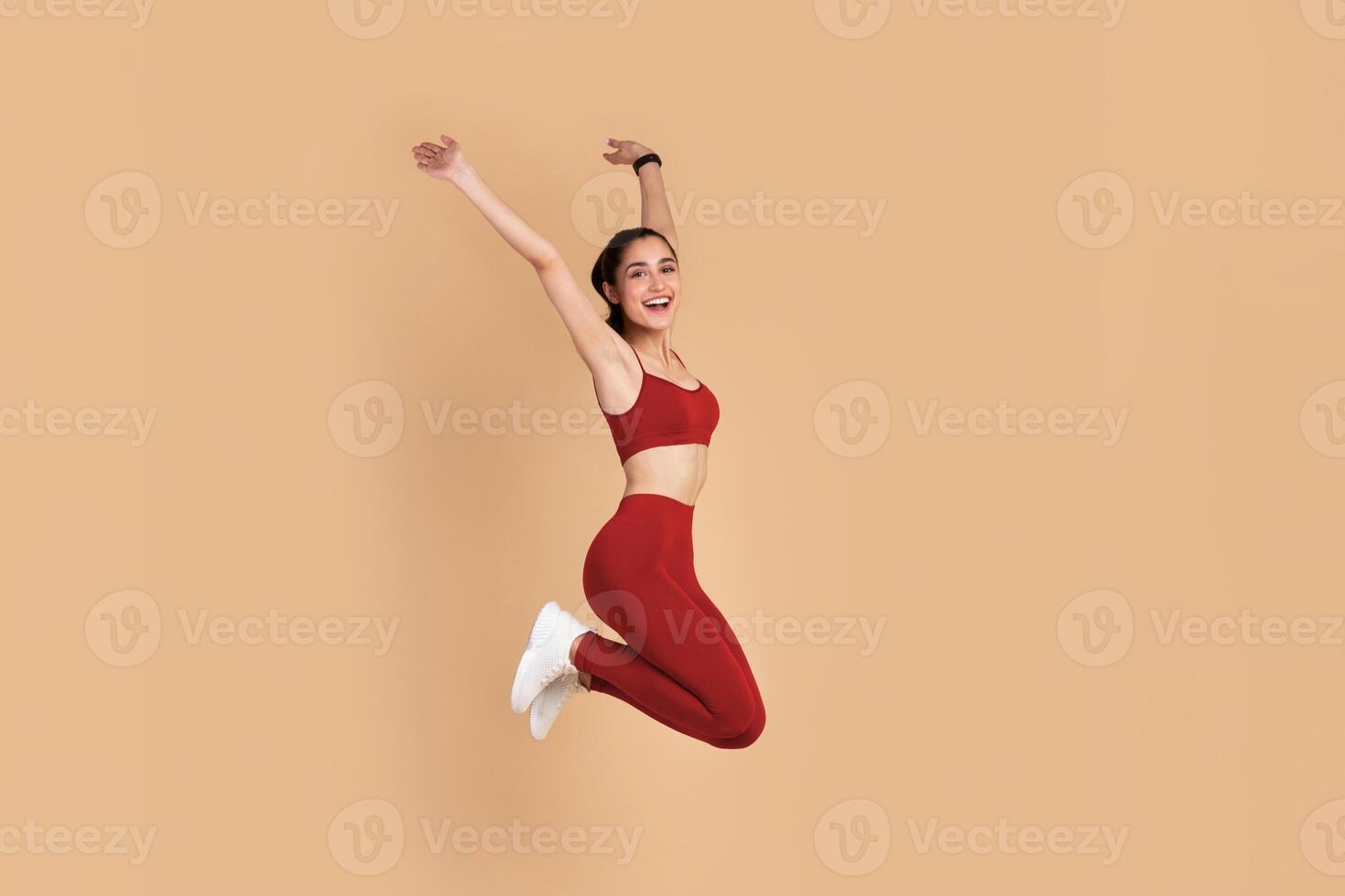 Full Length Portrait Of Happy Excited Smiling Young Woman In Sports Bra And Leggins Jumping Up And Raising Arms Up Isolated On Pastel Background, Celebrating Success, Studio Shot, Copy Space. photo