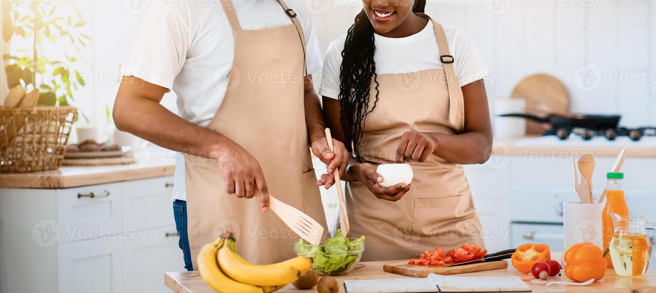 Young Happy African American Lovers In Aprons Cooking Together In Kitchen, Cheerful Black Couple Enjoying Preparing Healthy Food At Home, Adding Seasoning To Fresh Vegetable Salad, Free Space photo