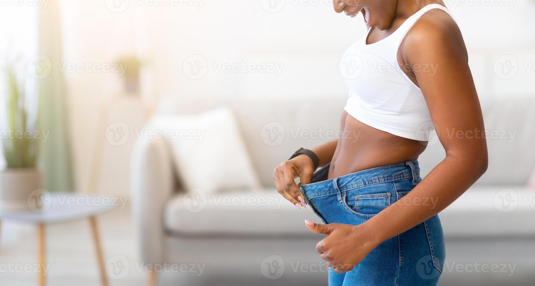 Excited Slim African Female Wearing Old Oversized Jeans Comparing Result Of Weight Loss Standing At Home. Slimming And Dieting Motivation, Before And After Comparison photo