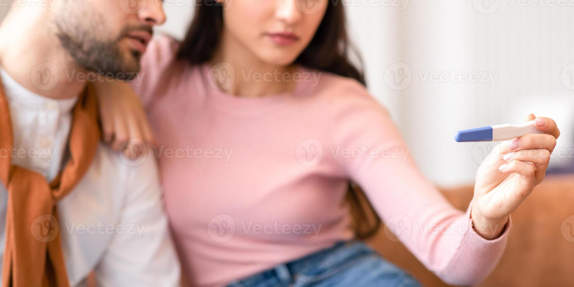 Depressed Arab Couple Holding Negative Pregnancy Test Sitting Together On Sofa At Home. Young Spouses Struggling Infertility And Dreaming To Be Parents. Childbirth Problem Concept. Selective Focus photo