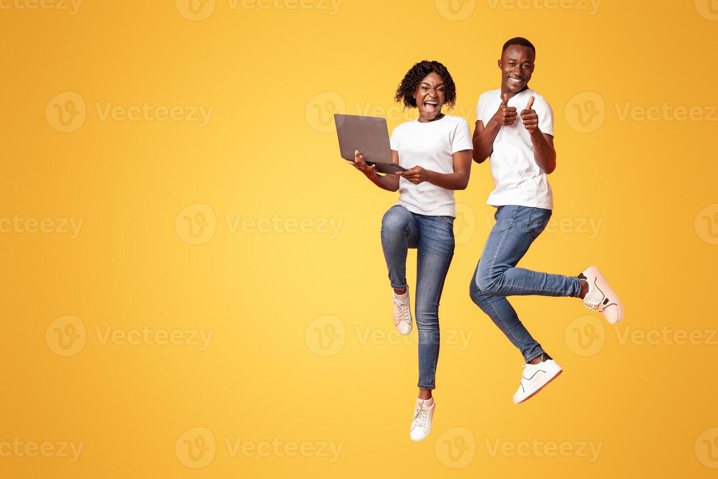 Happy african american millennial man and woman jumping up with laptop, shouting and gesturing on orange studio background. Young black couple gambling online successfully, using laptop, free space photo