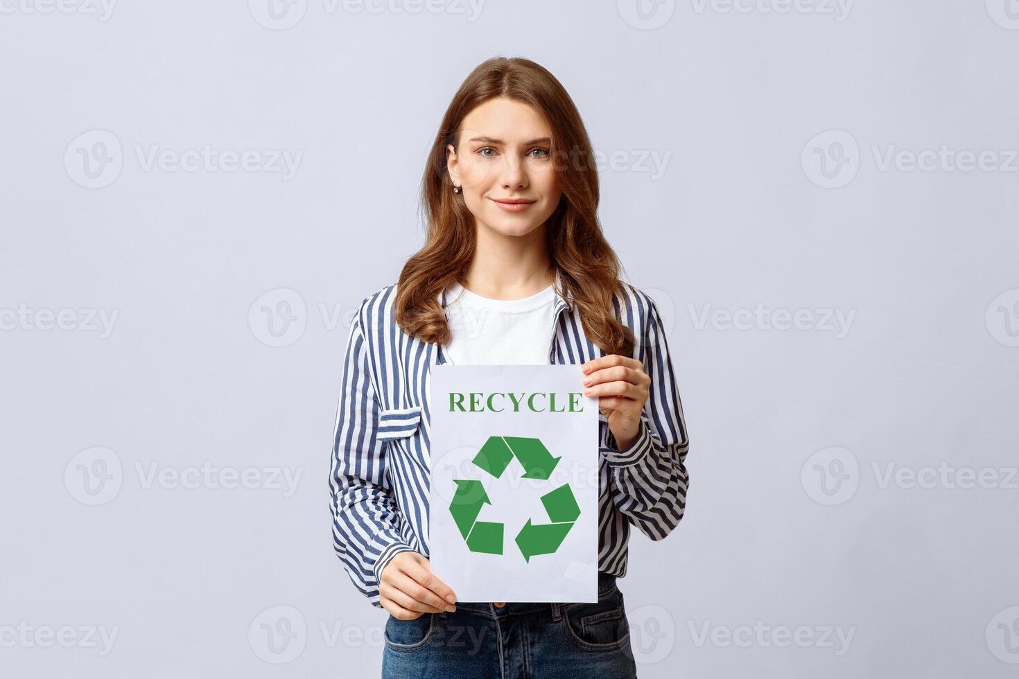 Millennial Eco-Activist Lady Showing Placard With Green Recycle Sign Icon, Promoting Save Environment, Smiling Nature Lover Woman Posing Over Light Studio Background, Looking At Camera, Free Space photo