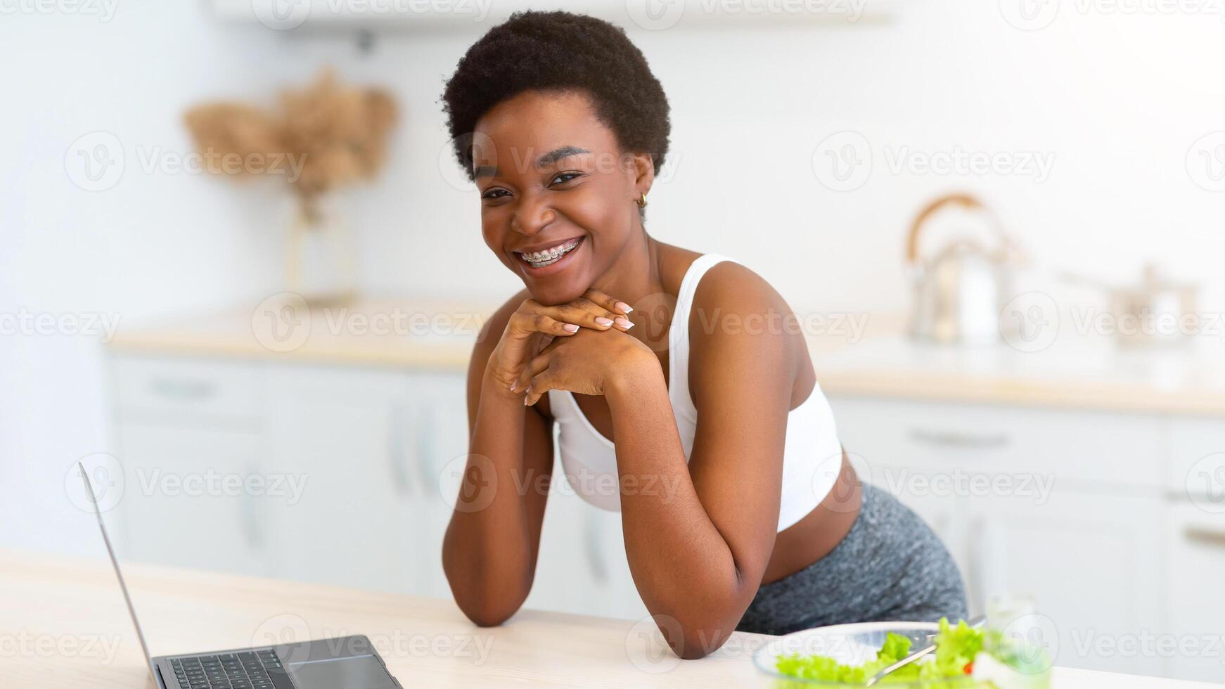 African American Woman Using Laptop Cooking And Browsing Healthy Food Recipes Online For Weight Loss Posing In Modern Kitchen At Home. Slimming And Dieting Website Concept photo