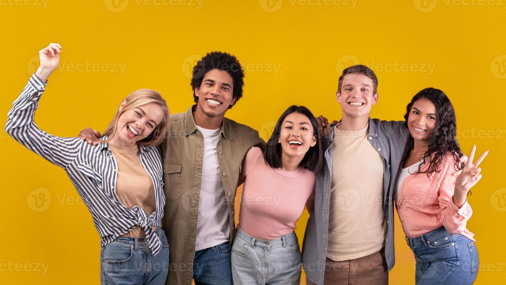 Friendship of international students and differ race pupils. Happy teens different people hugging, gesturing and expressing emotion of joy, isolated on orange background, studio shot, empty space photo