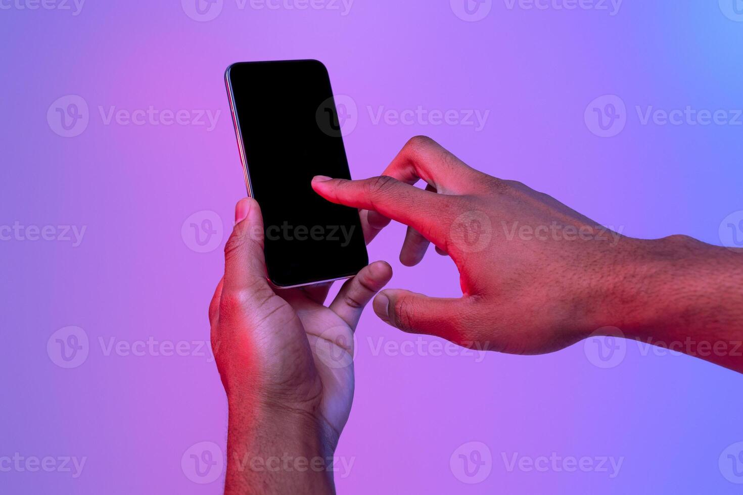 Male Hands Using Smartphone With Black Screen In Neon Light Over Purple Background, Unrecognizable African American Man Touching Phone Screen, Browsing New App Or Scrolling Website, Mockup Image photo