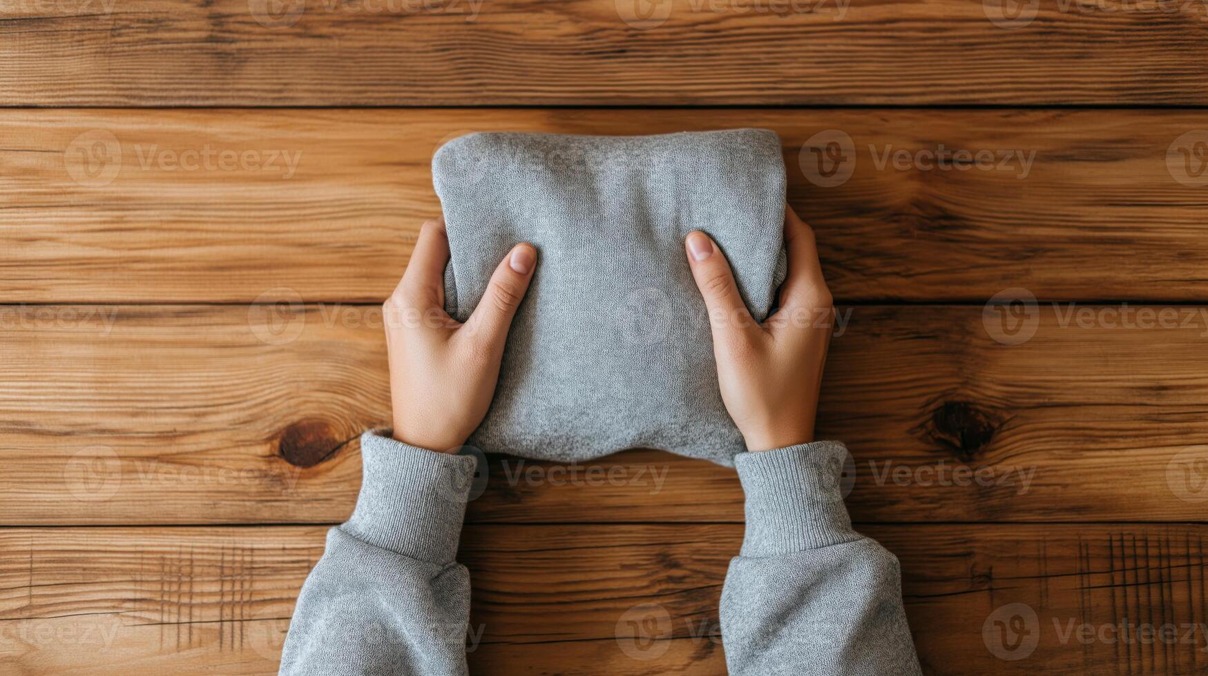 Two hands grasp a carefully folded gray sweater resting on a warm wooden surface. photo
