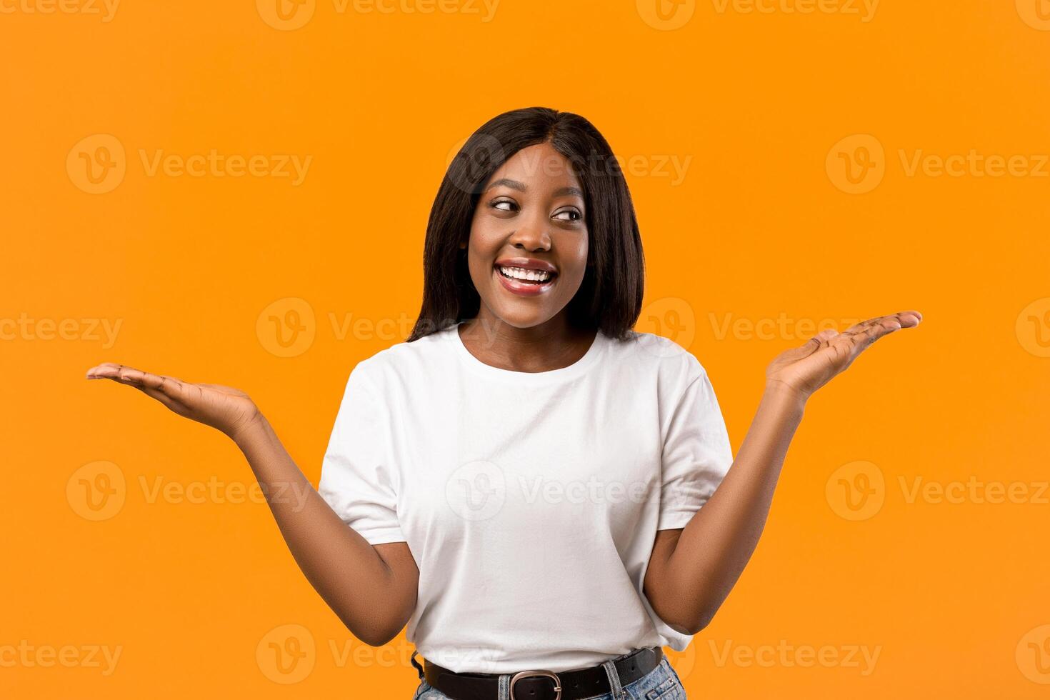 Confused black lady raising both hands up as holding something invisible on orange studio background, copy space. Smiling african american young woman showing or recommending something photo
